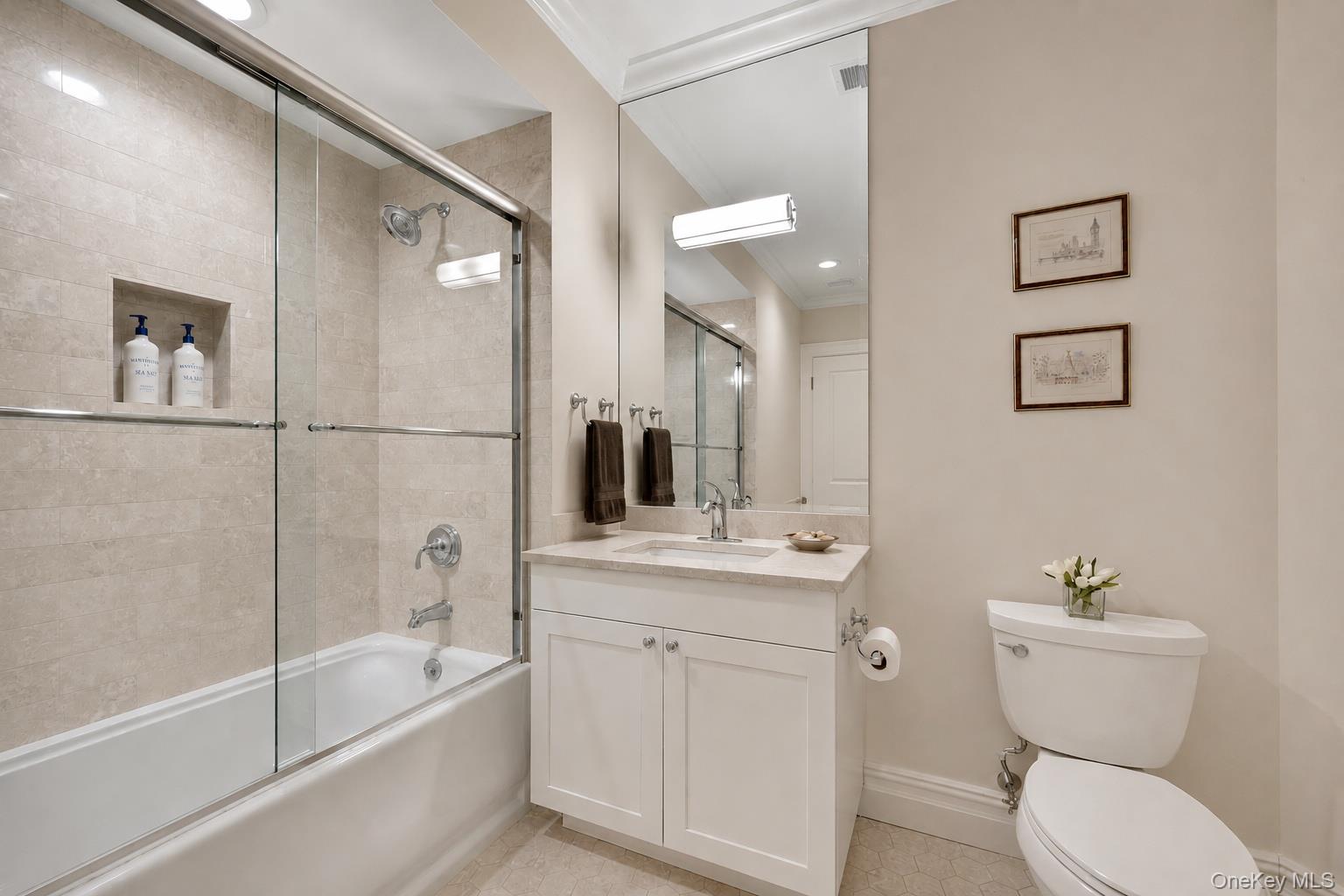 Bathroom with a glass-enclosed tub and shower, tiled walls, white vanity, and toilet.