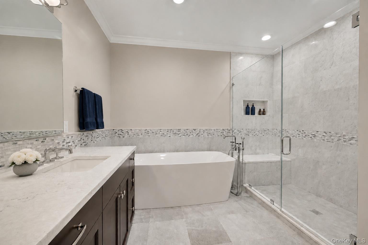 Bathroom with a freestanding tub, glass-enclosed shower, marble-look tile, and dark vanity.