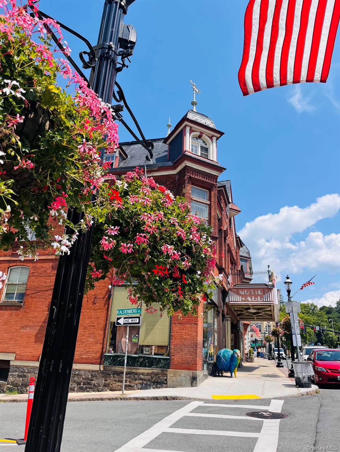 Historic red-brick commercial building with an ornate turret, Music Hall marquee, flowering planters, and an American flag.