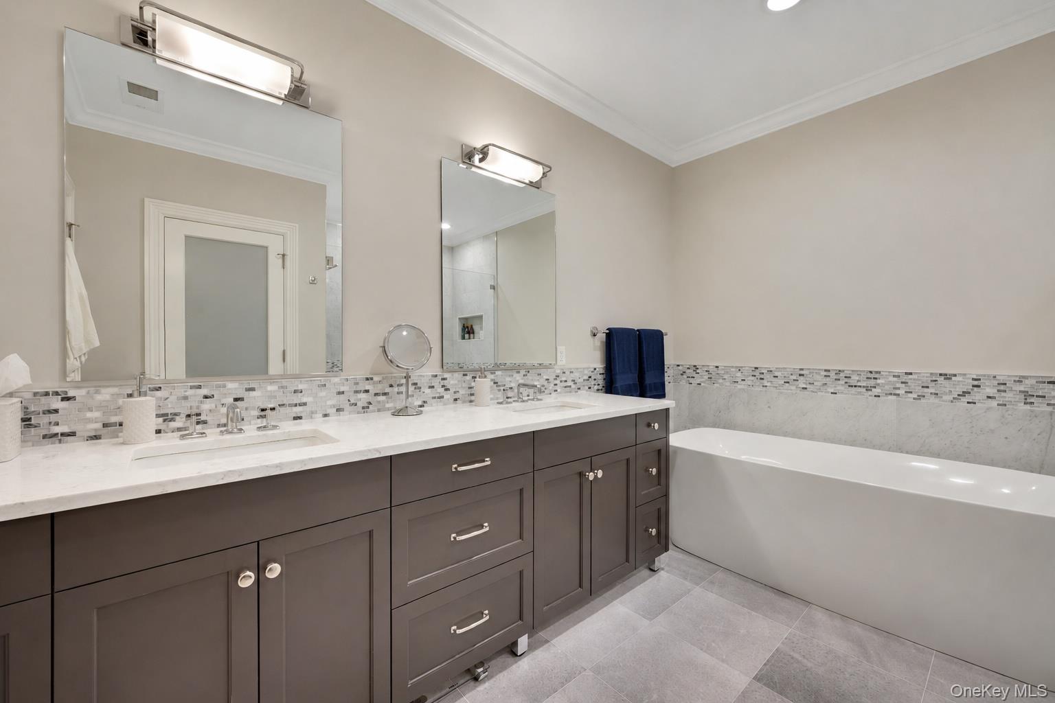 Bathroom with a long dark vanity, dual sinks, mirrored wall, and built-in bathtub.
