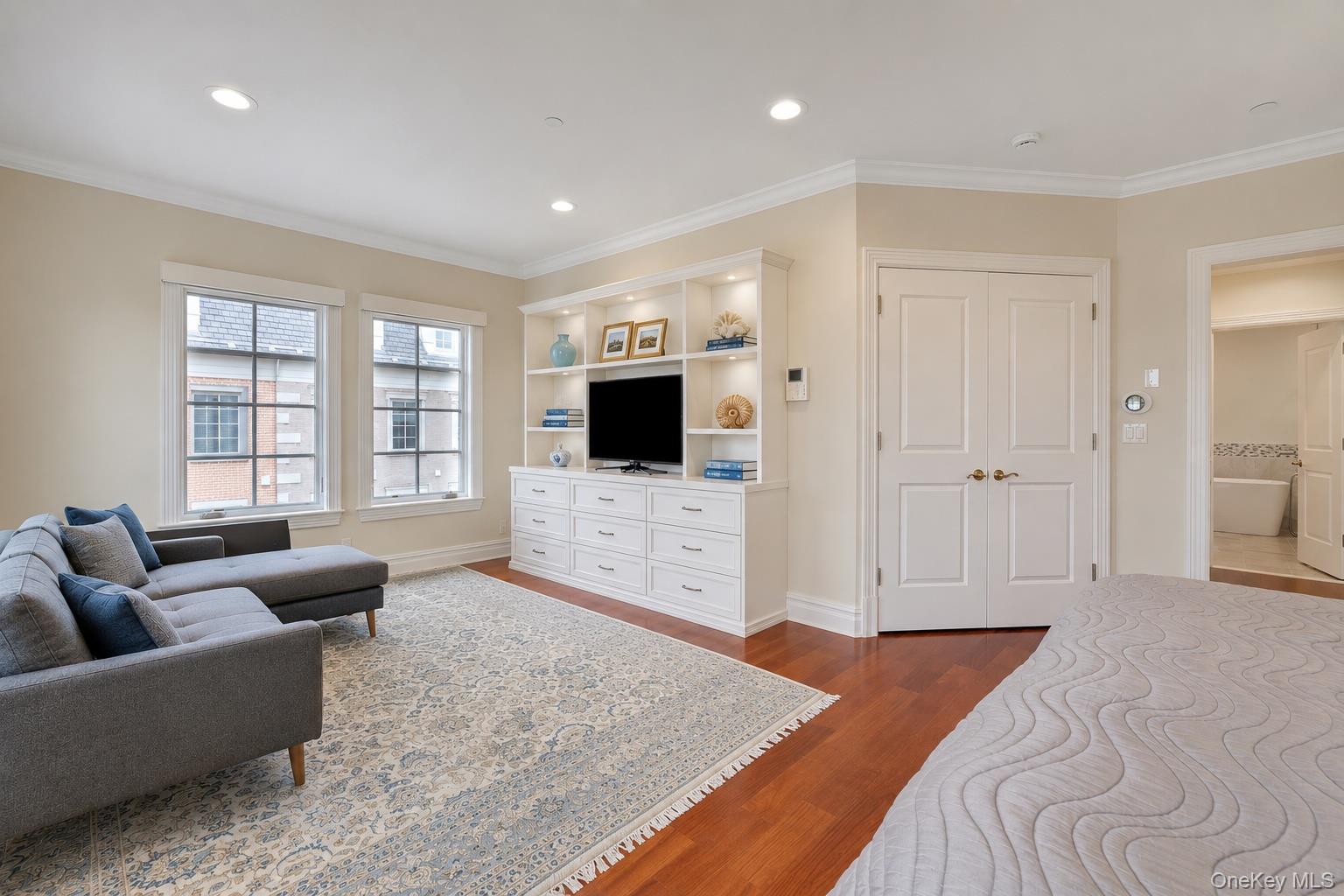 Bedroom with a gray bed and sofa, built-in television cabinet, and hardwood floors.