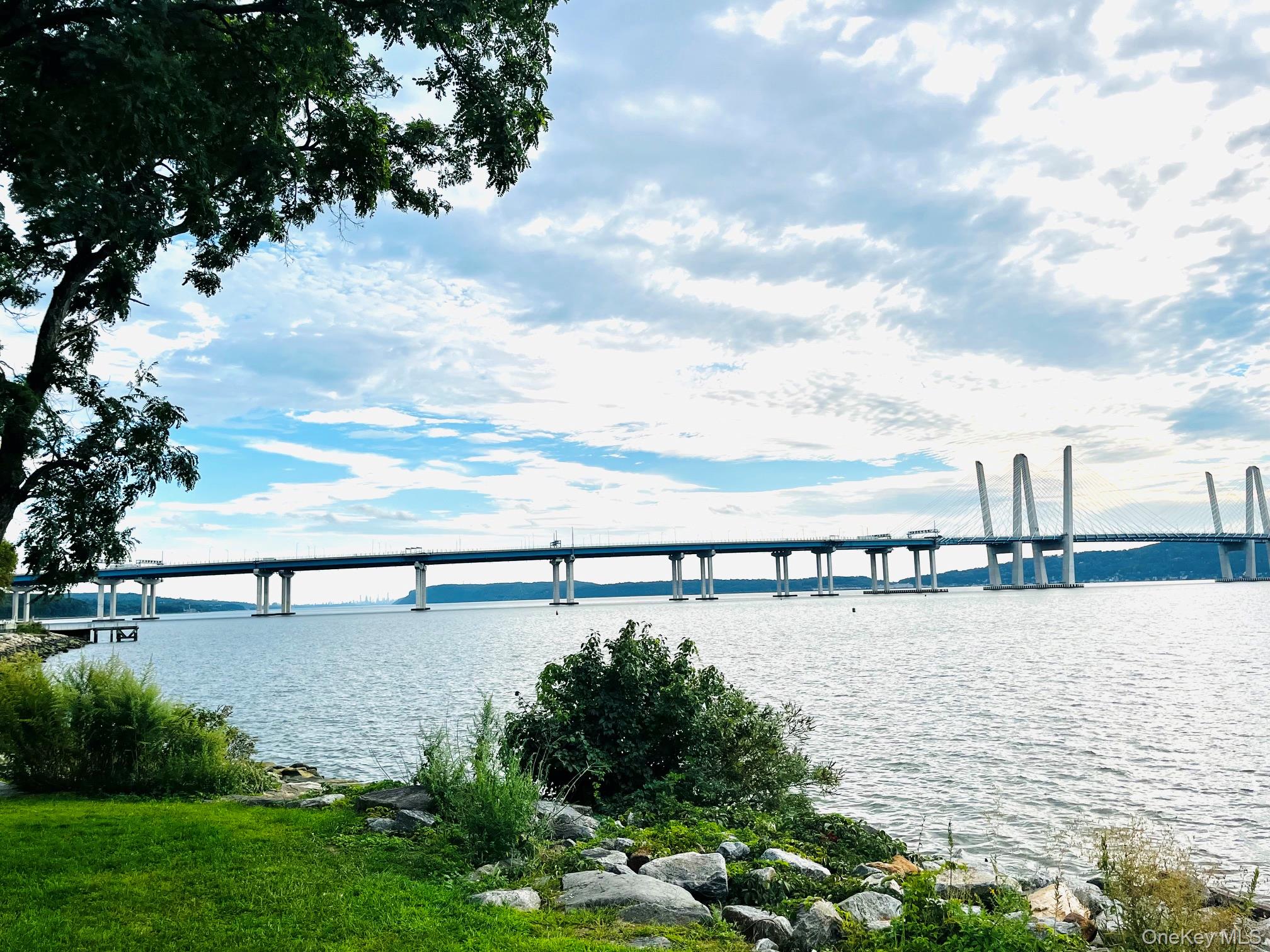 River and cable-stayed bridge viewed from a landscaped shoreline.