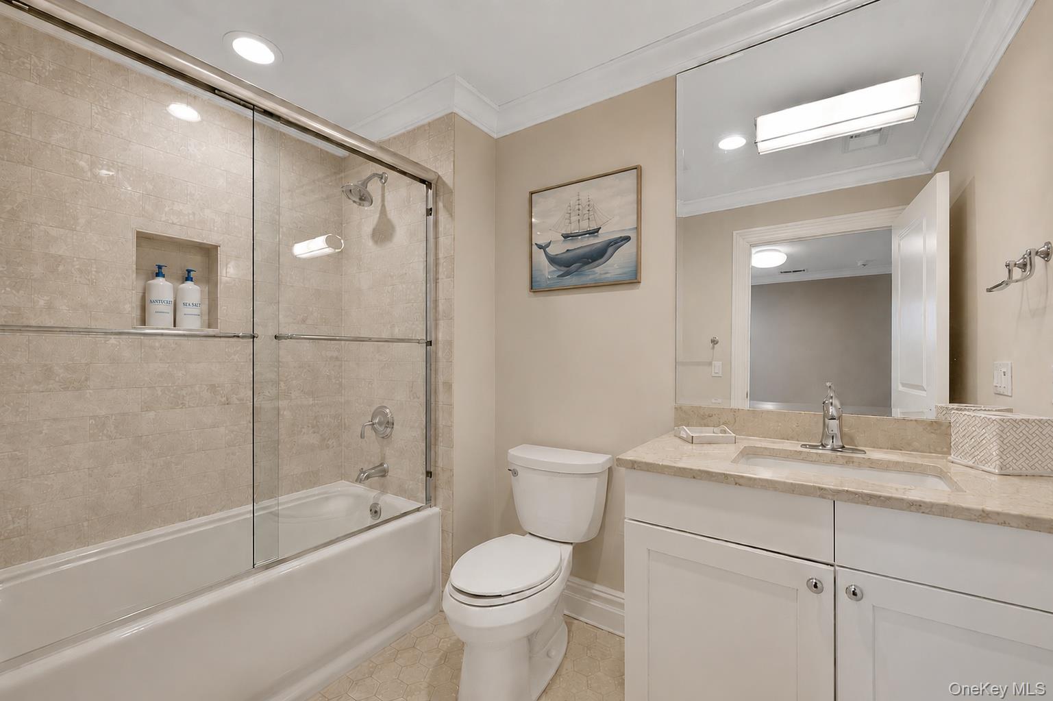 Bathroom with a glass-enclosed tub, beige tile, white vanity, and framed whale artwork.