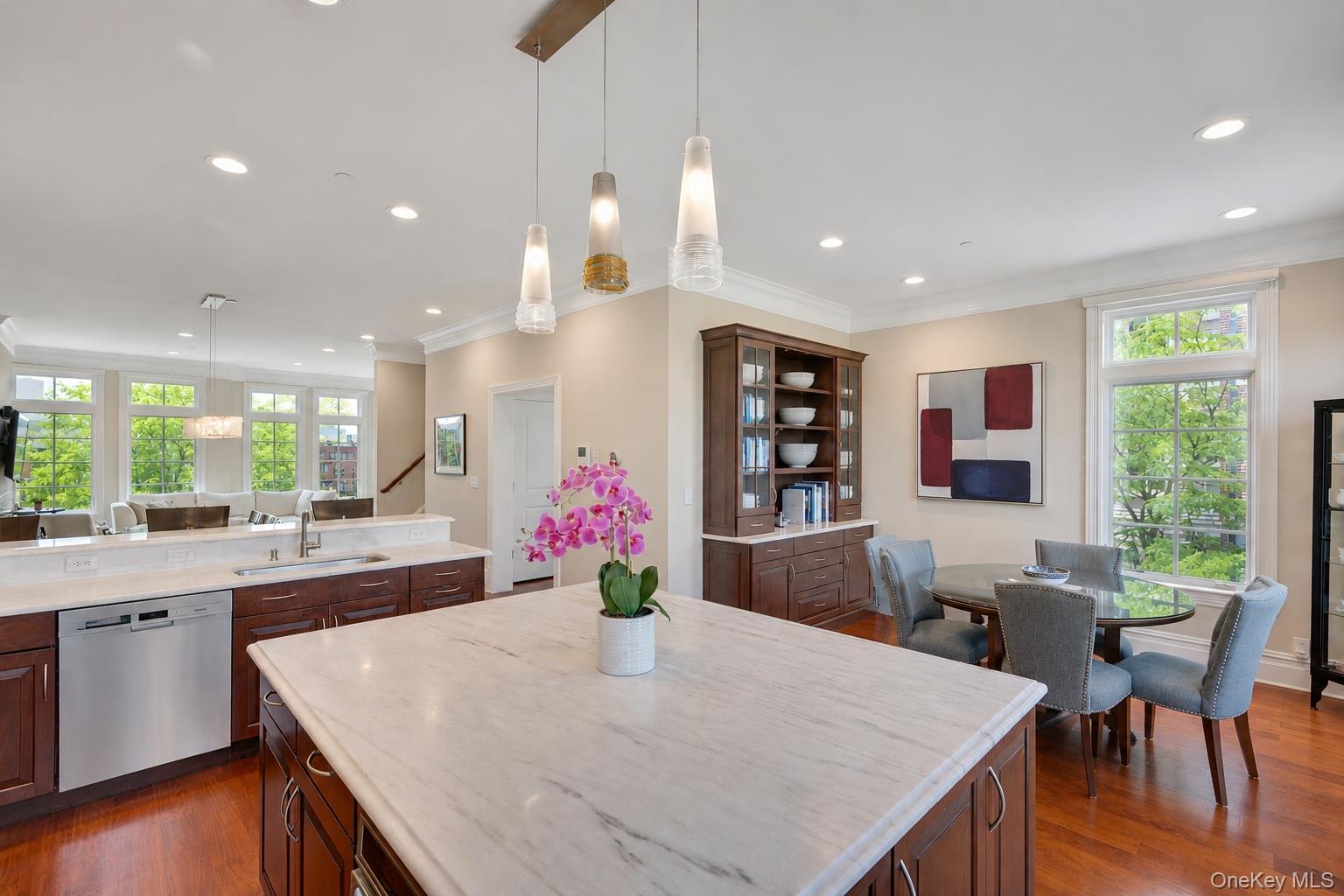 Open kitchen and dining area with a large marble island, dark cabinetry, and tall windows.