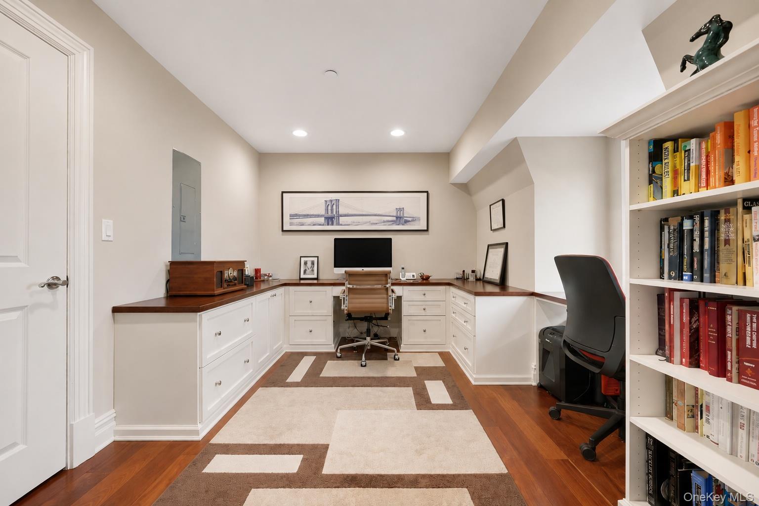 Home office with a built-in desk, white cabinetry, and book-filled shelves.