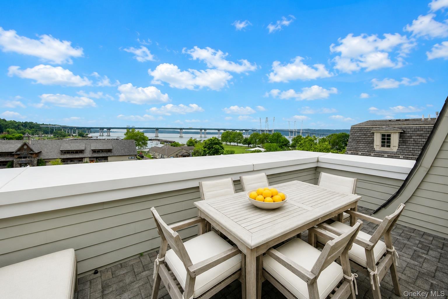 Rooftop terrace dining area overlooking a river and long bridge.