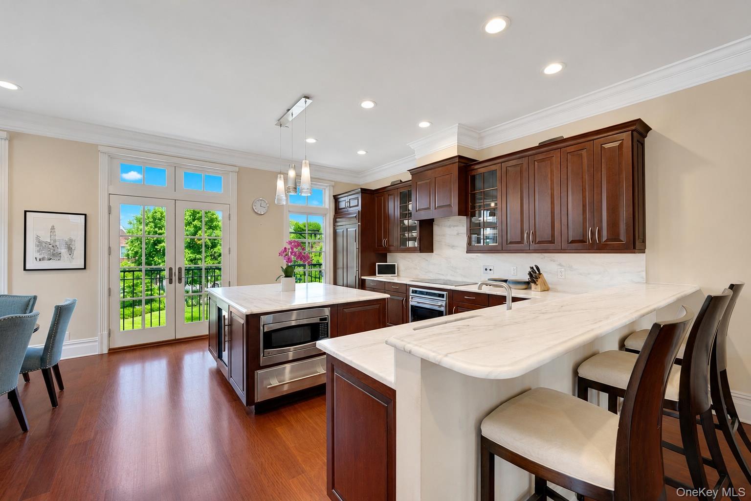 Kitchen with dark wood cabinets, marble counters, a large island, and French doors opening to greenery.