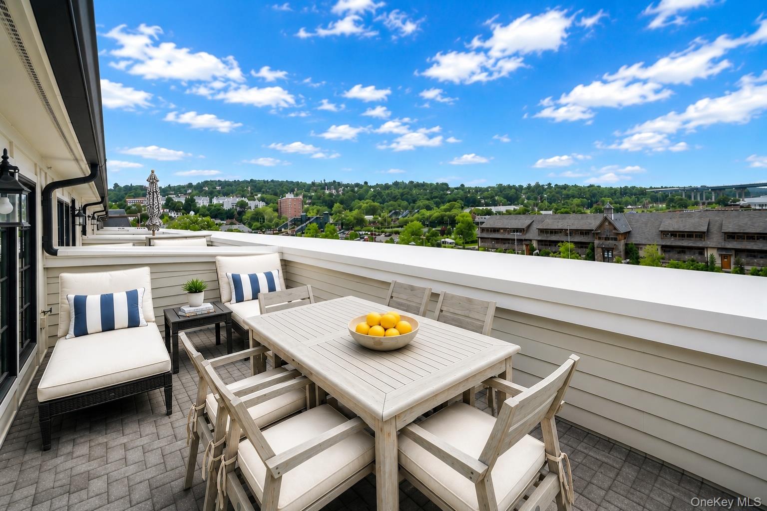 Rooftop terrace with a furnished dining area and views over a green hillside neighborhood.
