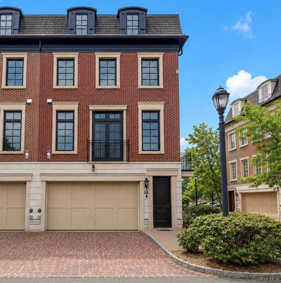 Red-brick townhouse with a mansard roof, double garage, and brick-paved driveway.