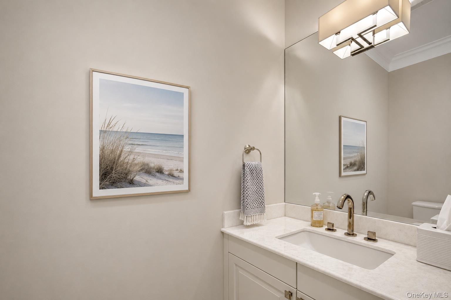 Bathroom vanity with marble countertop, brass fixtures, and framed beach prints.