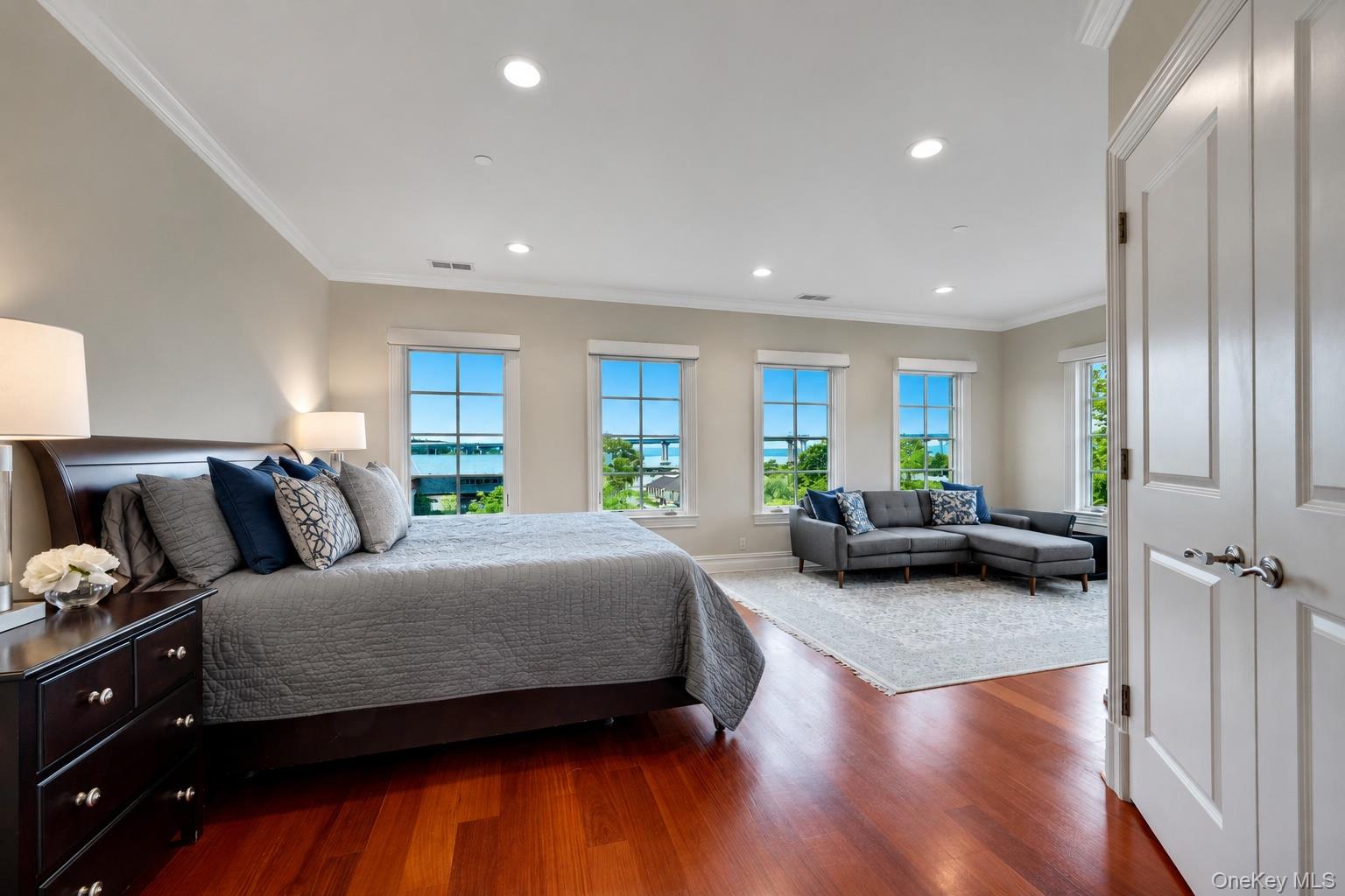 Bedroom with a large bed and sitting area overlooking the water through several windows.