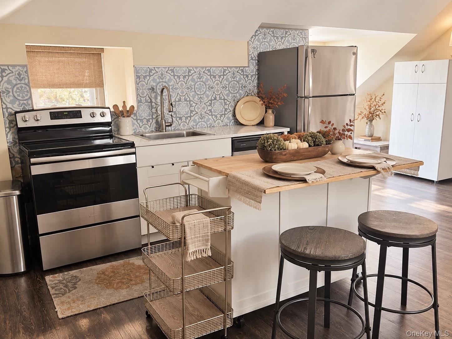Staged kitchen with a wood-topped island, patterned tile backsplash, and stainless-steel appliances.