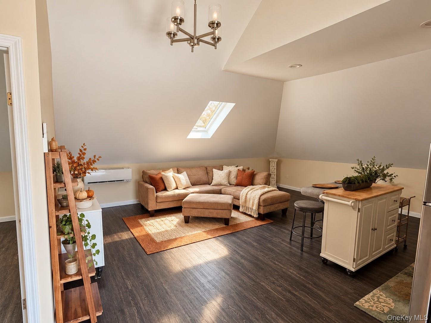 Living room with a tan sectional beneath a sloped ceiling and skylight, beside a small kitchen island.