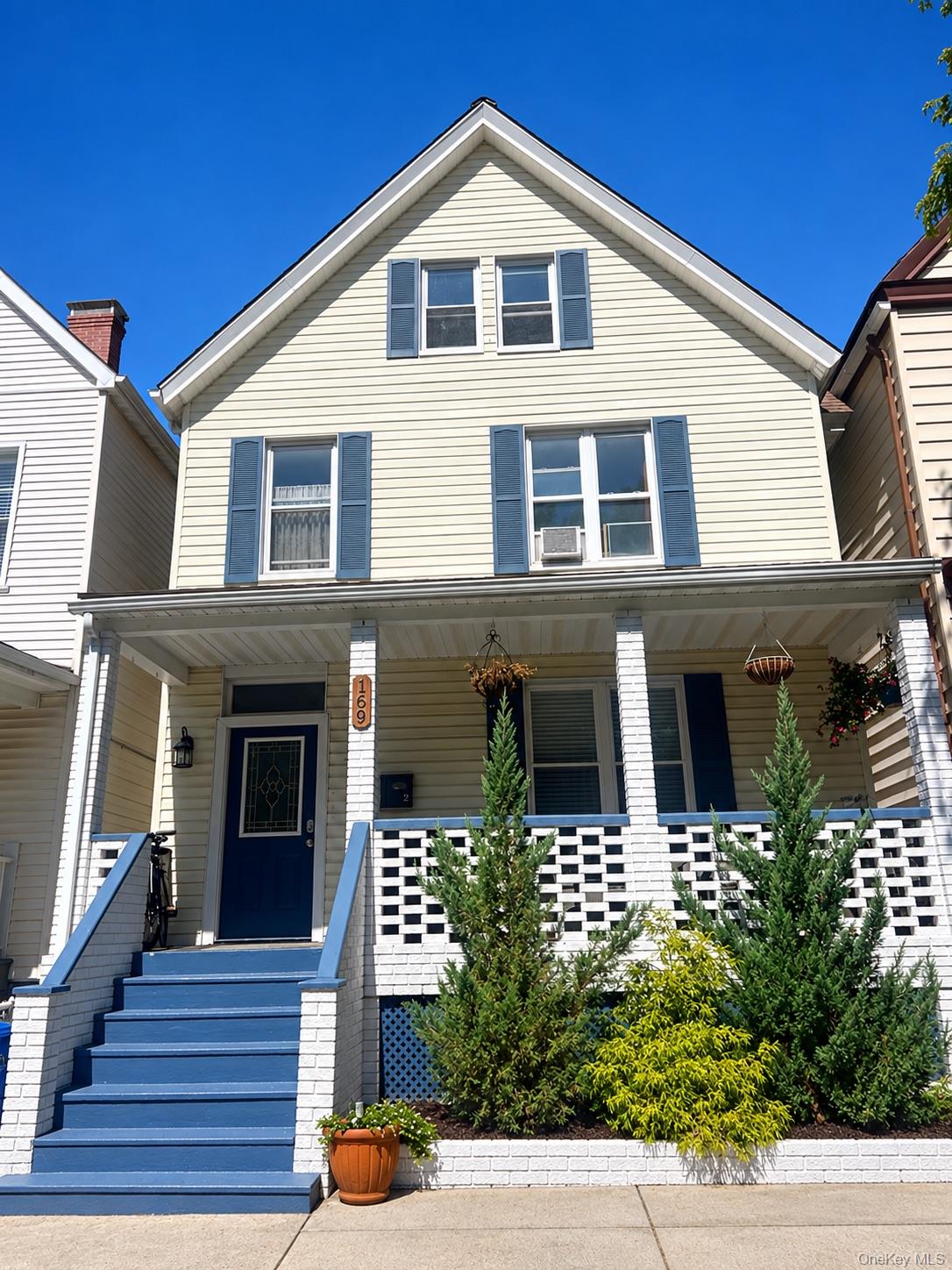 Cream-sided house with blue shutters, a covered porch, blue steps, and landscaped shrubs.