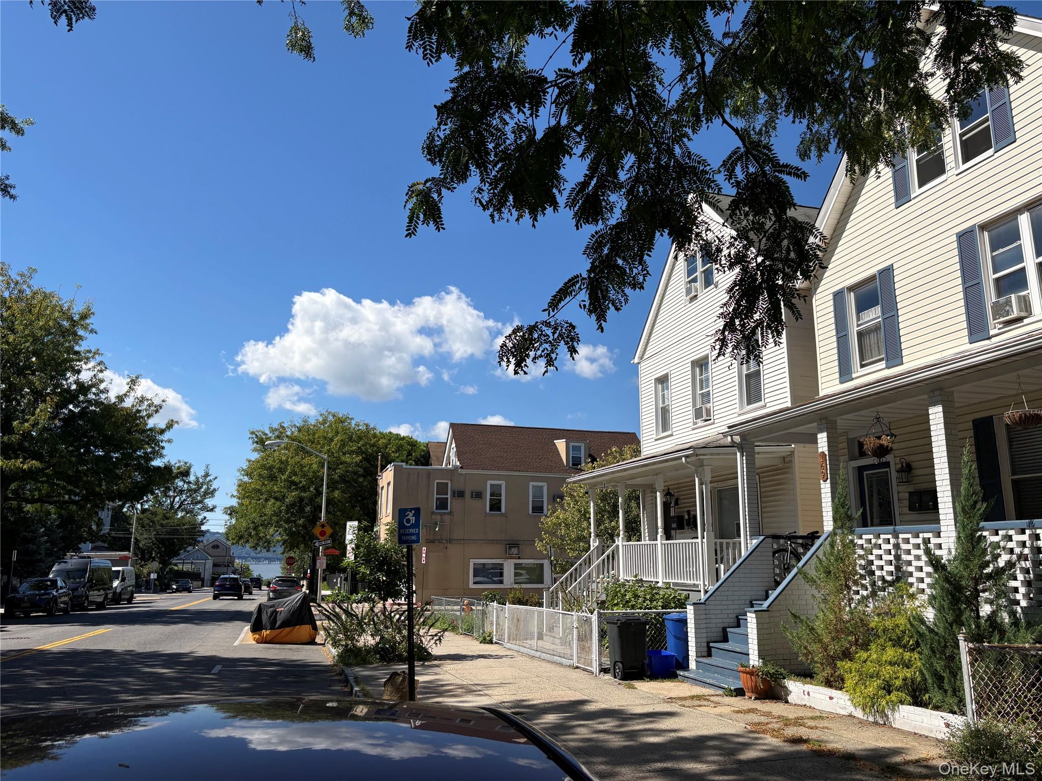 Multi-story house with blue shutters and a covered porch on a tree-lined residential street.
