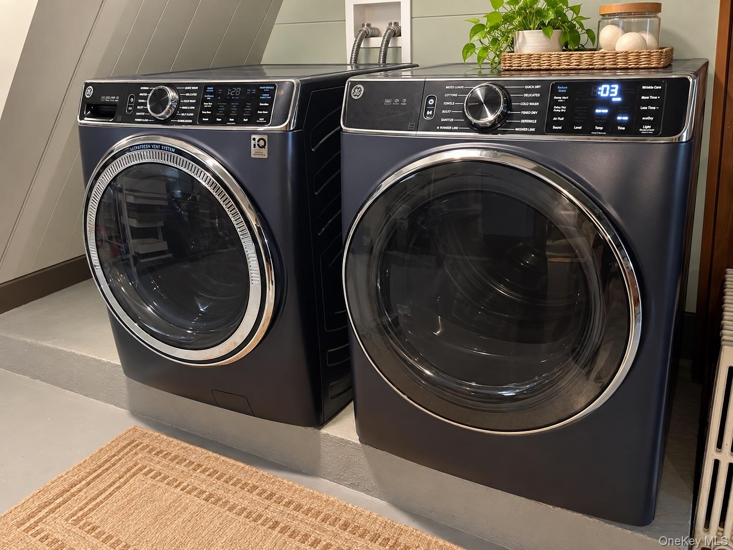 GE washer and dryer in a laundry room, with a plant and basket on top.