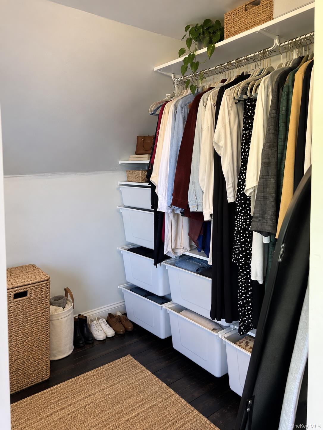 Walk-in closet with hanging clothes, white storage bins, woven baskets, and dark wood flooring.