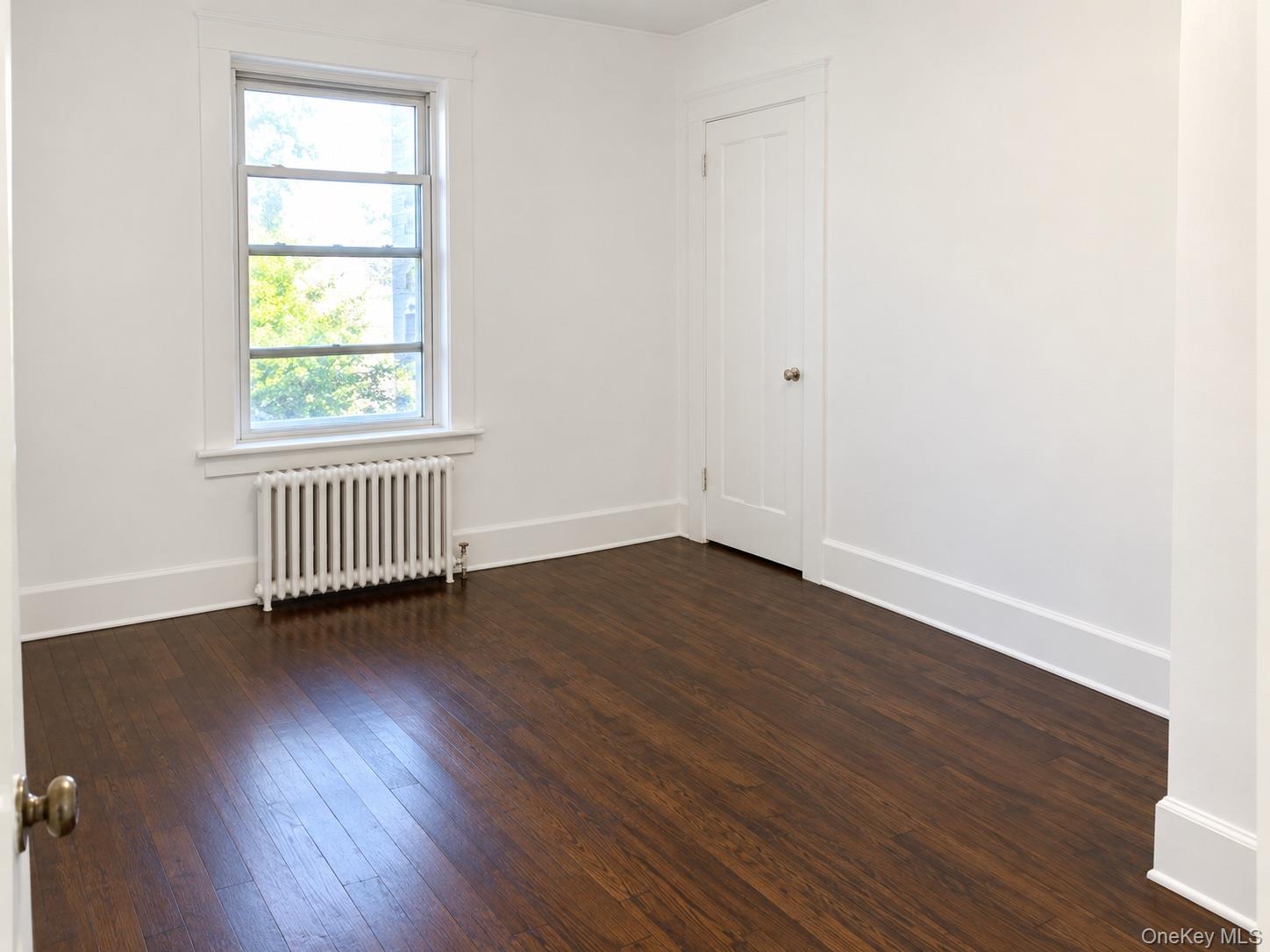 Empty room with dark hardwood floors, a tall window, and a radiator.