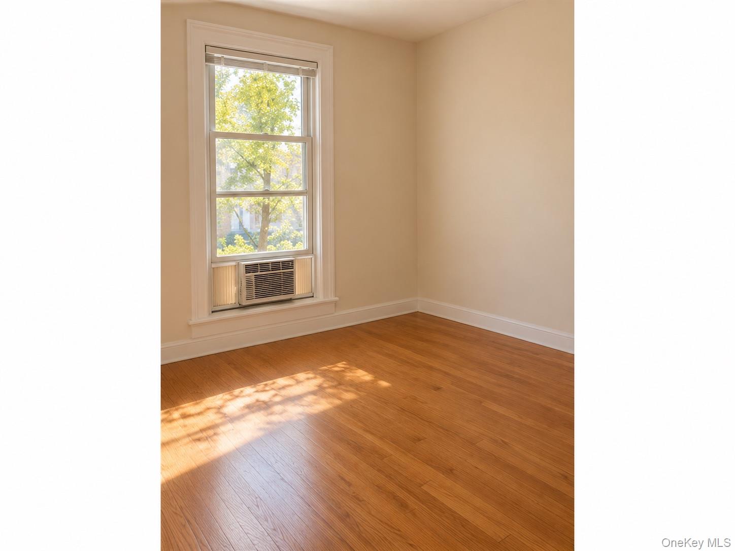 Empty room with hardwood floors, a tall window, and a window air conditioner.