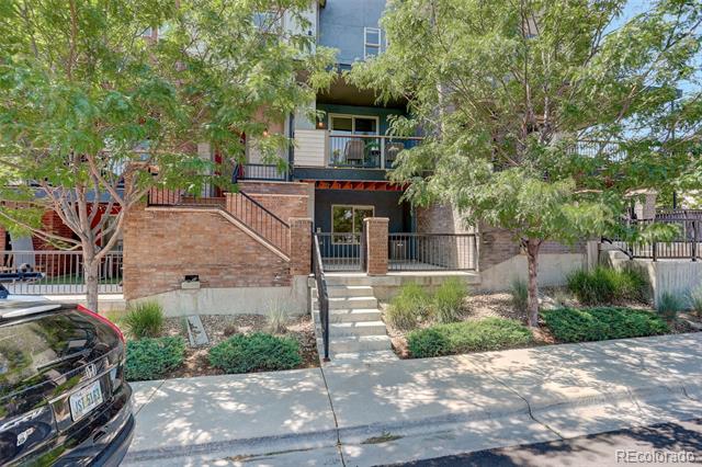 Residential building entrance with brick walls, front steps, balconies, and leafy sidewalk trees.