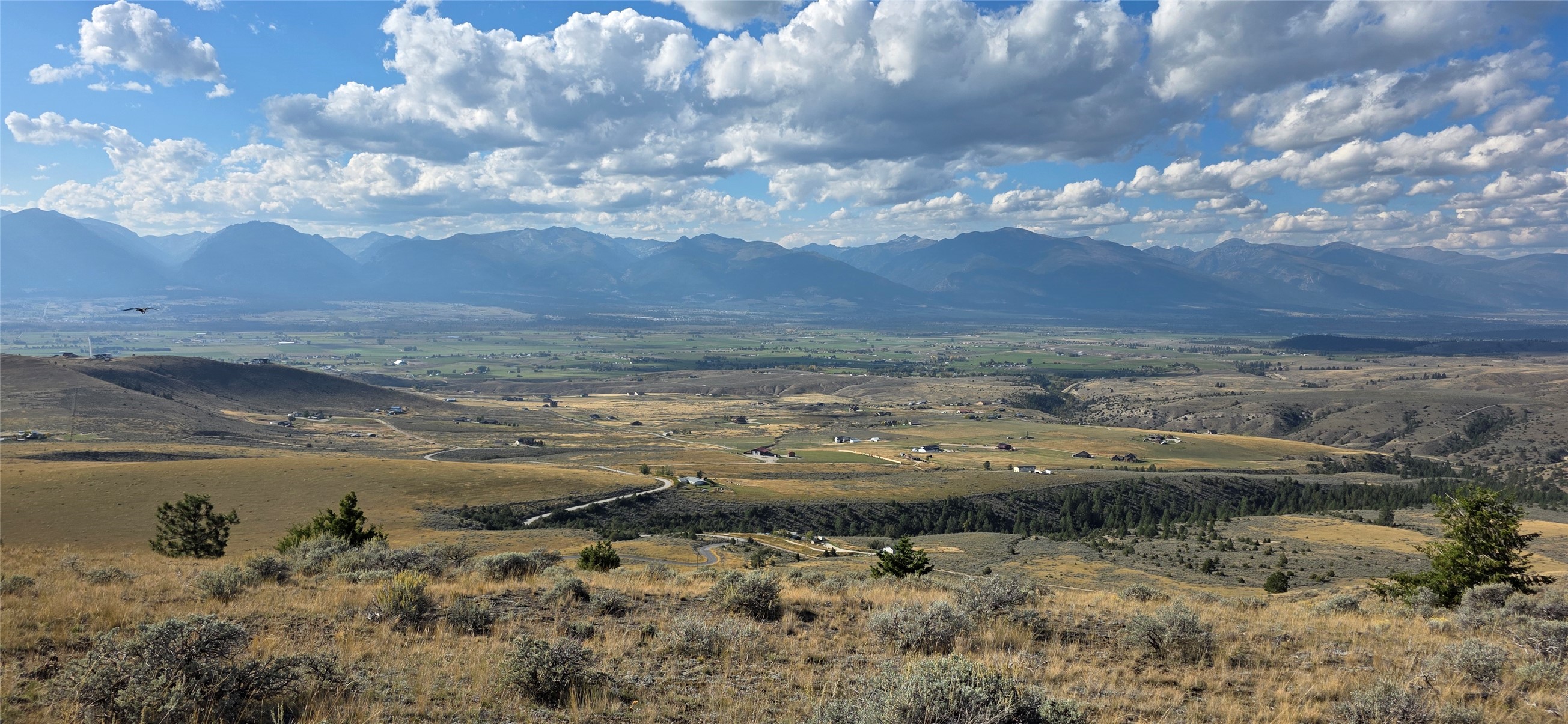 Vacant rolling land overlooks a broad valley and distant mountain range beneath a cloud-filled sky.