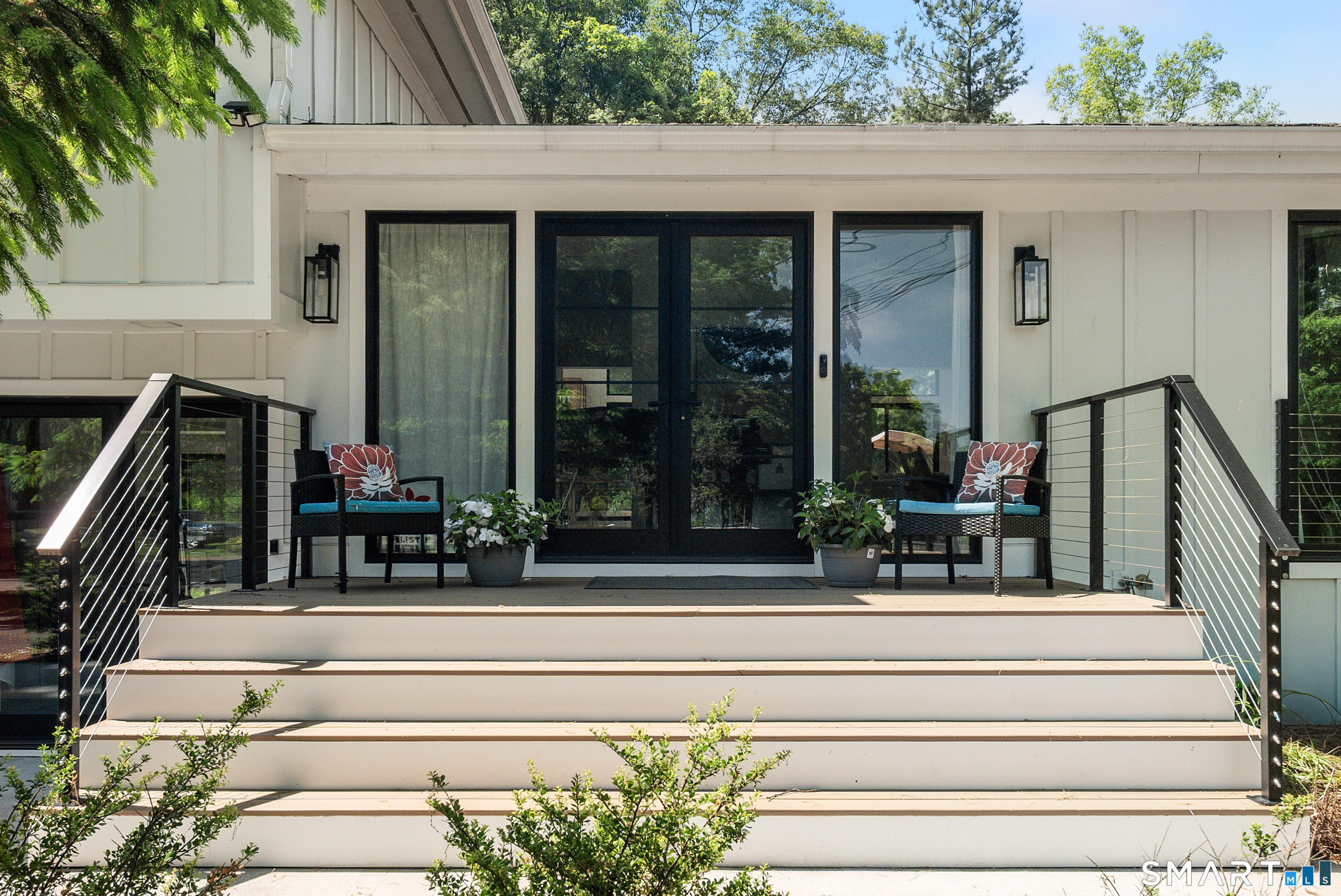 Modern white house entry with wide steps, black railings, glass doors, and porch seating.