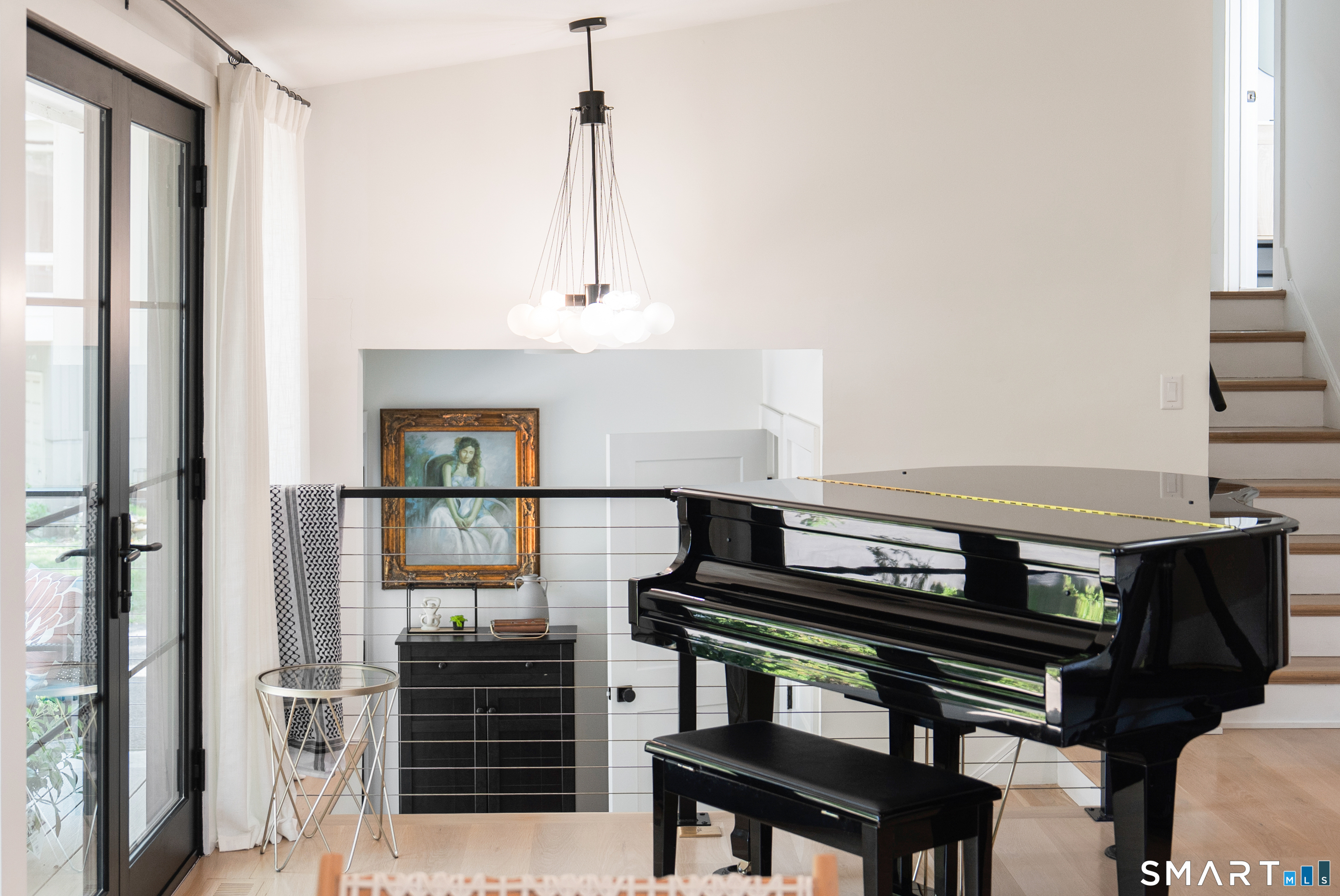Black grand piano in a bright living area beside a glass door and staircase.