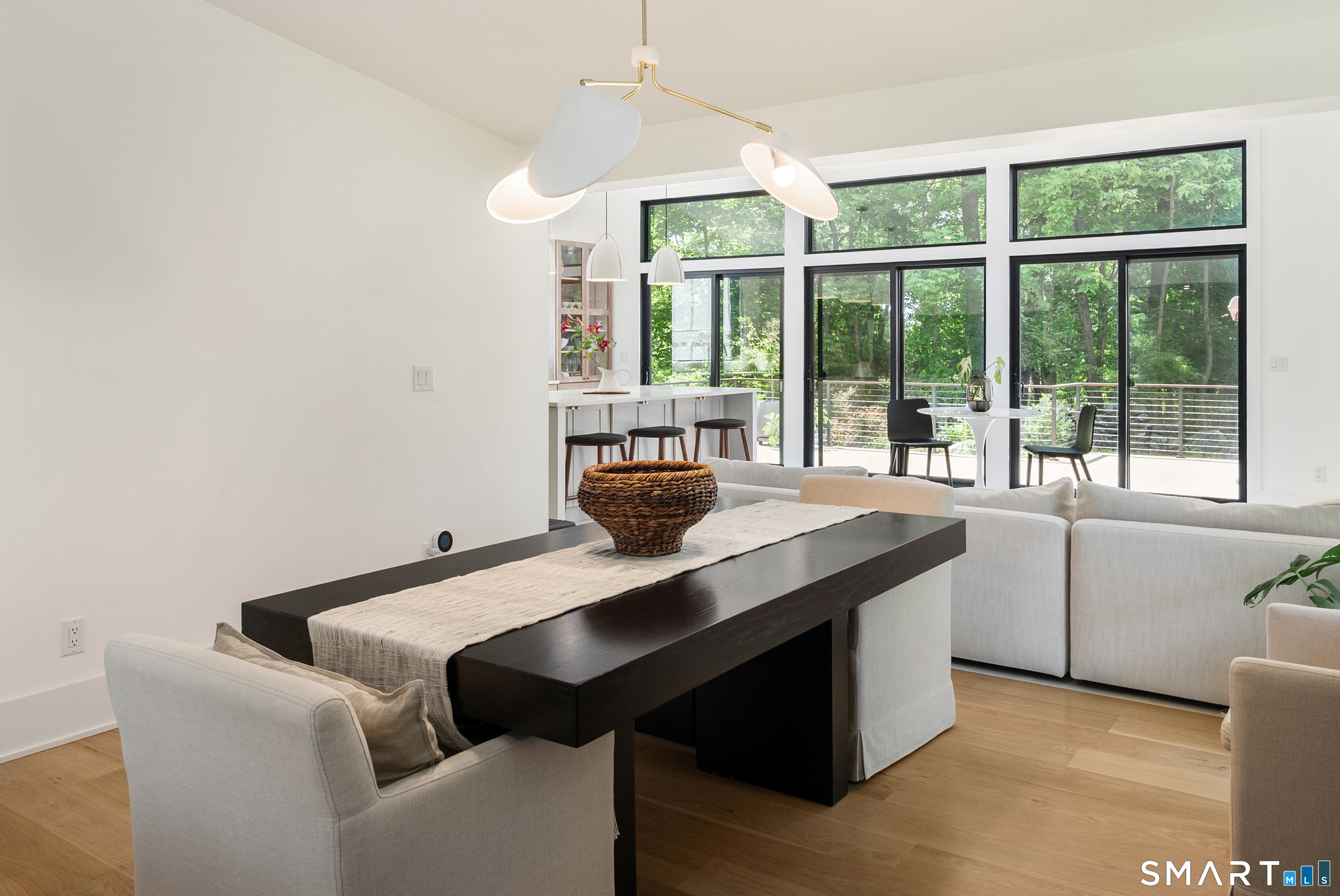 Open-plan living and dining area with modern furnishings and large windows overlooking leafy trees.
