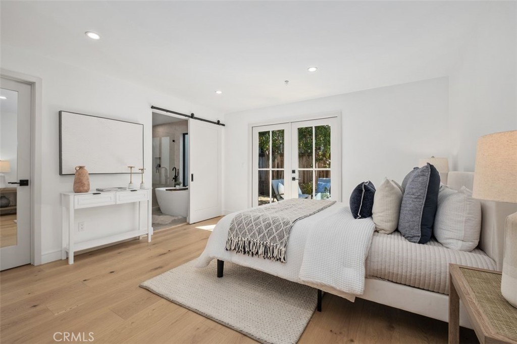 Bright bedroom with a white bed, light wood floors, and French doors opening to a small outdoor area.