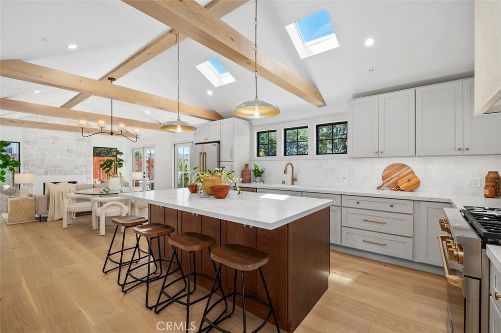 Open-plan kitchen with a large island, wood cabinetry, bar stools, and exposed ceiling beams.