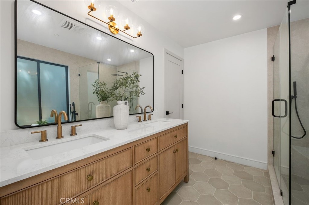 Bathroom with fluted wood double vanity, brass faucets, large mirror, and glass-enclosed shower.