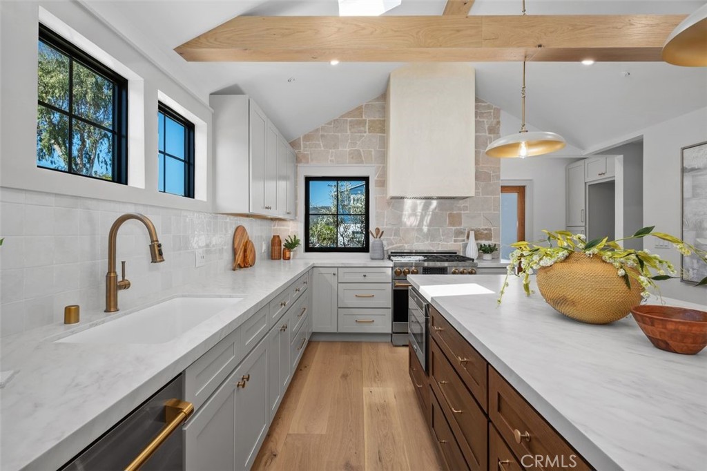 Bright kitchen with a wood-front island, white counters, brass fixtures, and black-framed windows.