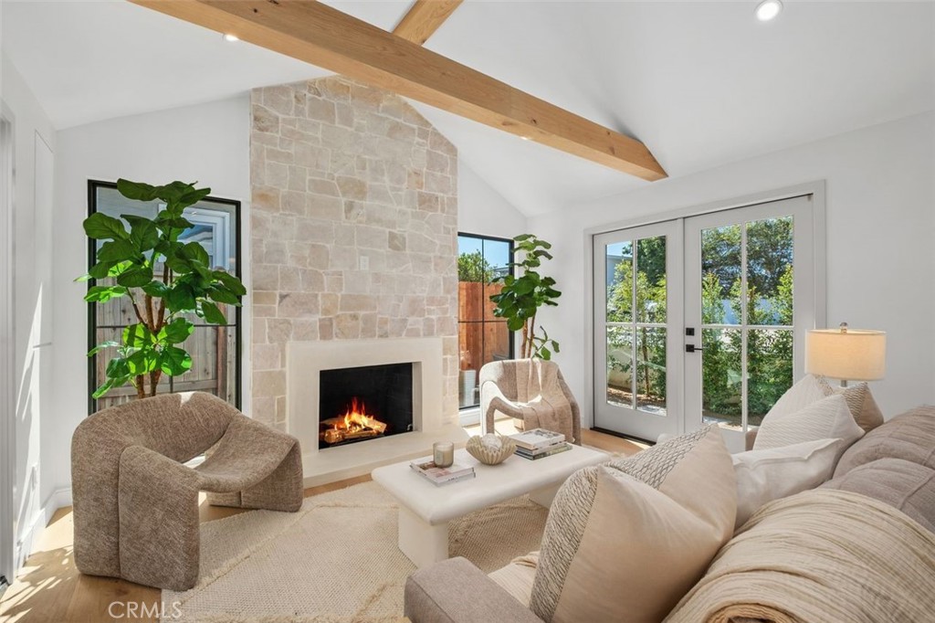 Living room with a stone fireplace, exposed wood beam, and glass doors overlooking greenery.