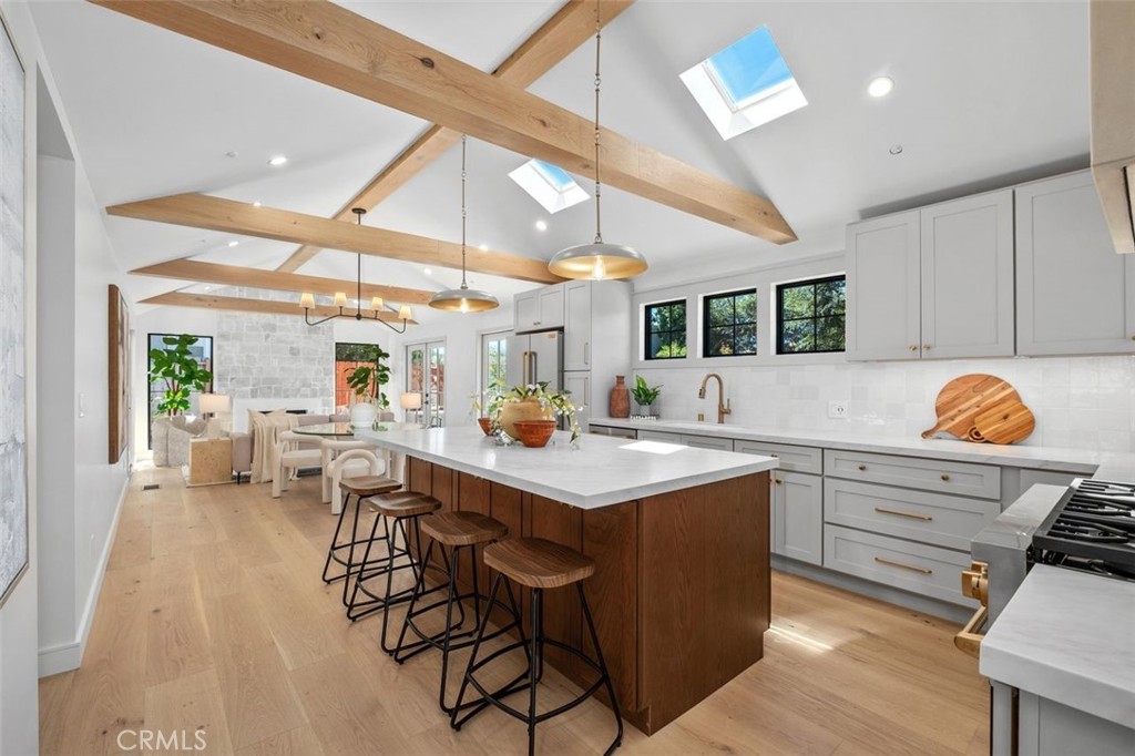 Open-plan kitchen with a wood-front island, white cabinetry, exposed beams, and skylights.
