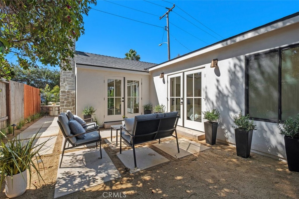Outdoor patio with black lounge seating, stone pavers, white walls, and French doors.