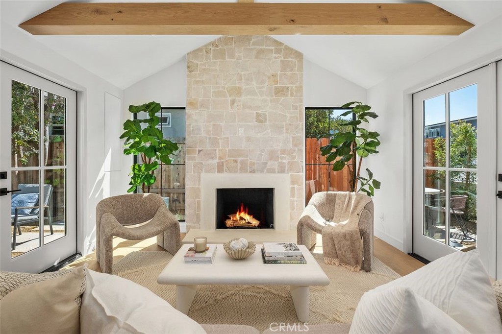 Living room with a tall stone fireplace, exposed wood beam, and glass doors to the outdoors.