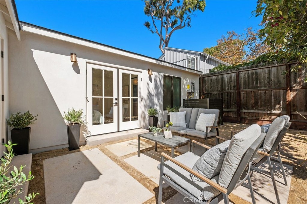Private backyard patio with gray lounge furniture, French doors, and a tall wooden fence.
