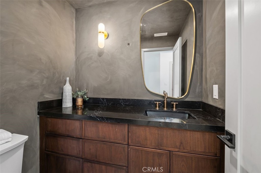 Bathroom vanity with dark stone counter, walnut drawers, brass fixtures, and a rounded mirror.