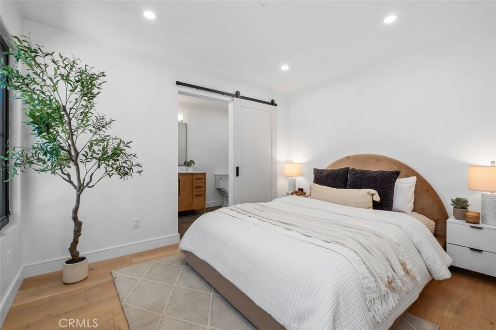 Staged bedroom with a rounded wood headboard, white bedding, and a sliding barn door to the bathroom.