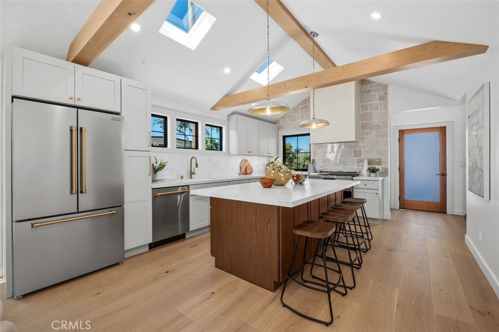 Kitchen with a large island, bar stools, stainless steel appliances, and exposed timber ceiling beams.