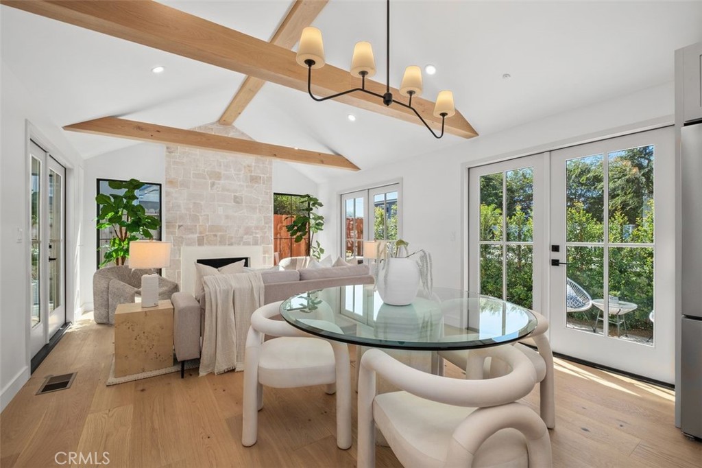 Dining and living room with exposed wood ceiling beams, a stone fireplace, and glass doors to greenery.