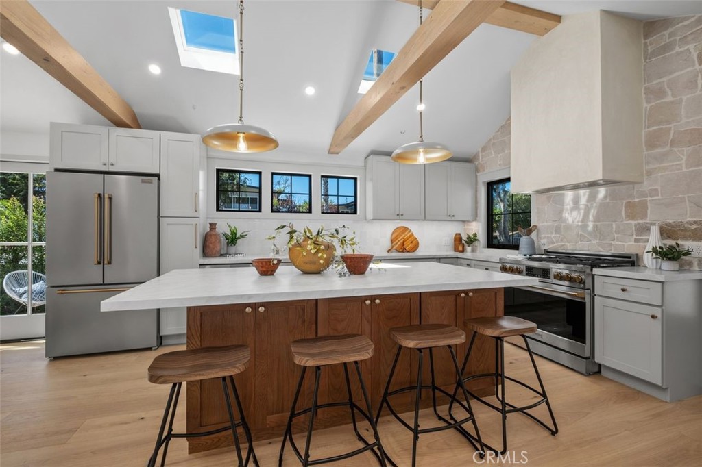 Bright kitchen with a stone island, walnut cabinetry, skylights, and exposed wooden ceiling beams.