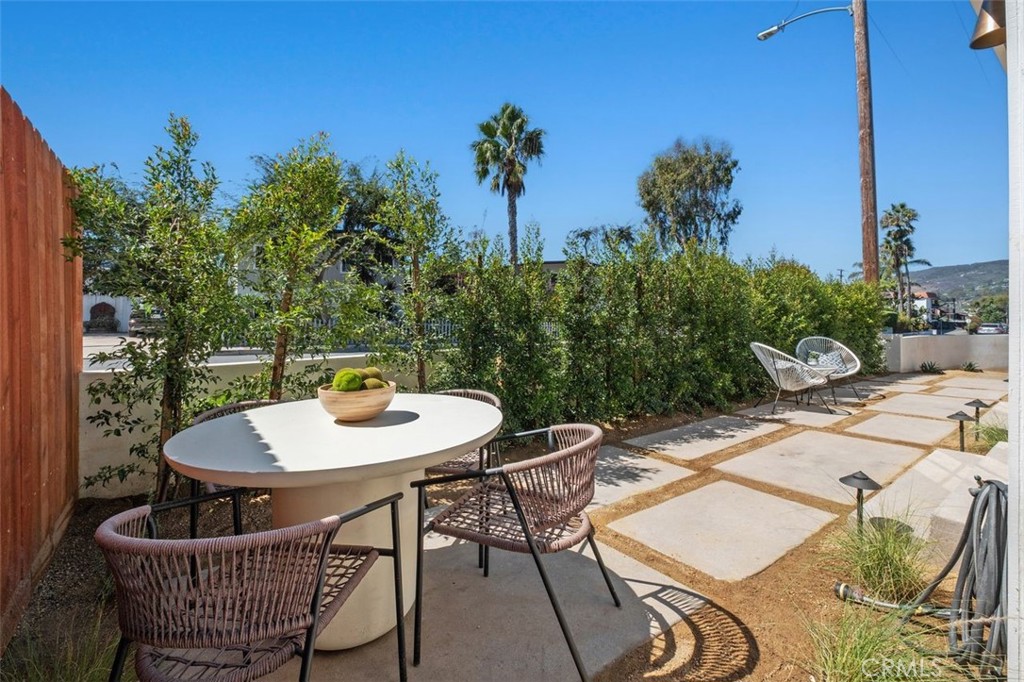 Outdoor patio with a round dining table, woven chairs, and leafy privacy hedge.