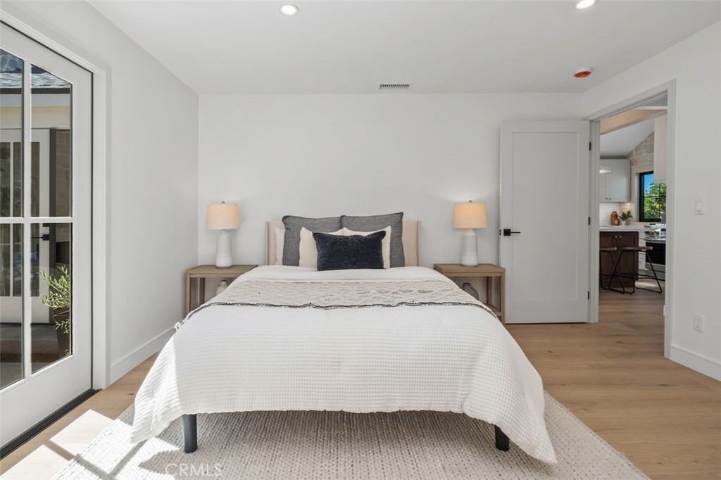 Staged bedroom with a white-covered bed, matching bedside lamps, sliding glass doors, and wood floors.