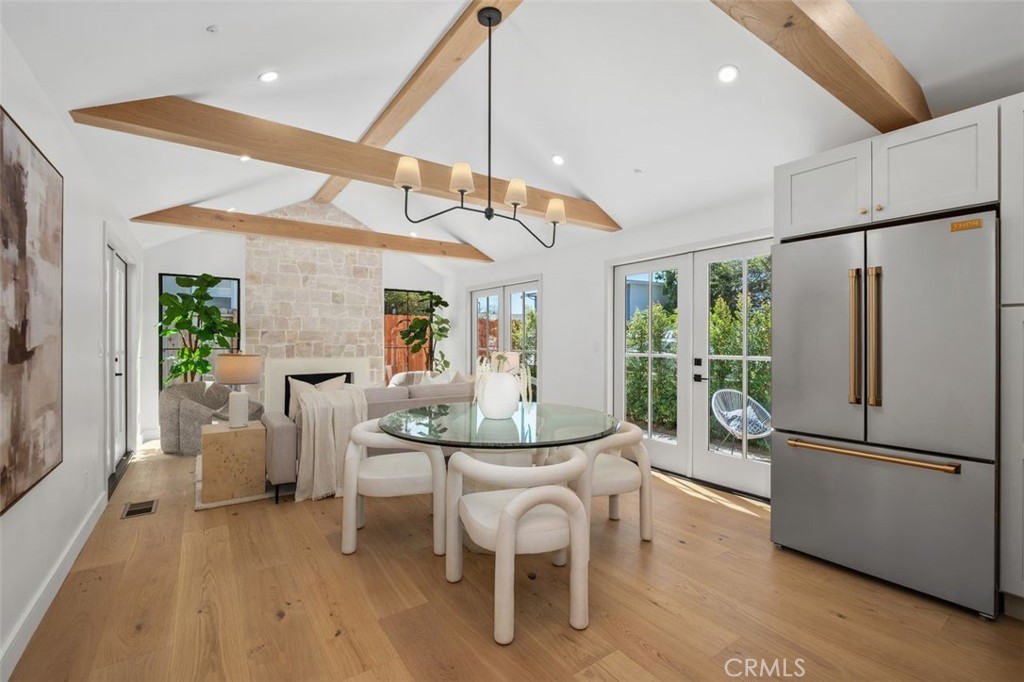 Open-plan dining and living area with a glass table, stone fireplace, and exposed wood ceiling beams.