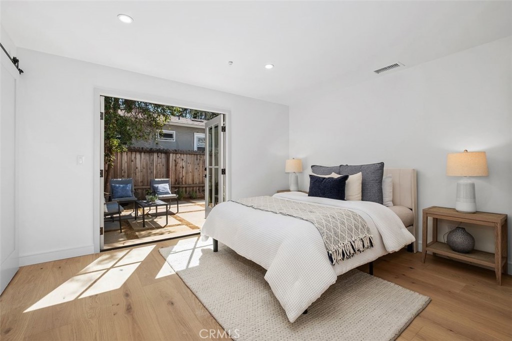 Staged bedroom with white bedding and open French doors to a fenced patio.