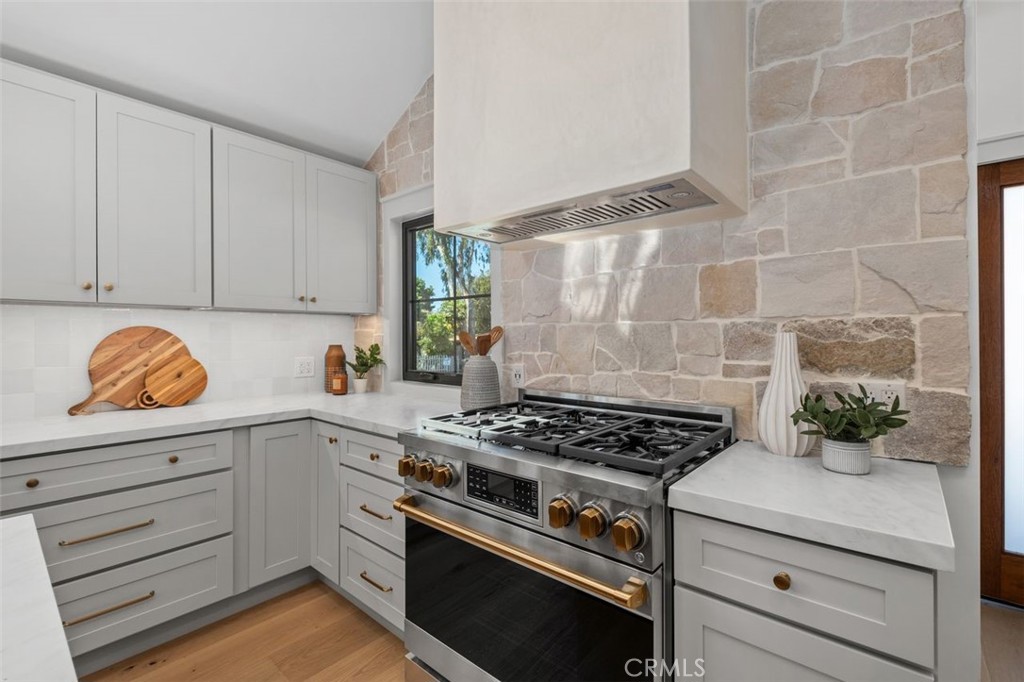Kitchen with a brass-accented stainless range and pale stone backsplash.