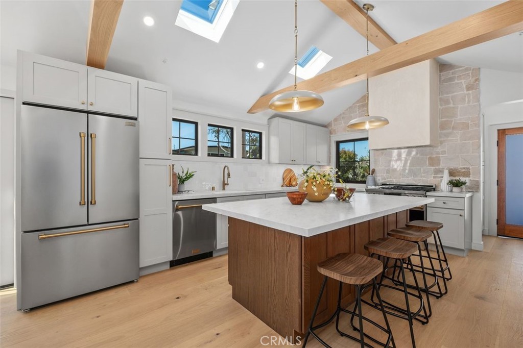 Kitchen with a large wood island, white stone countertop, stainless steel appliances, and exposed ceiling beams.