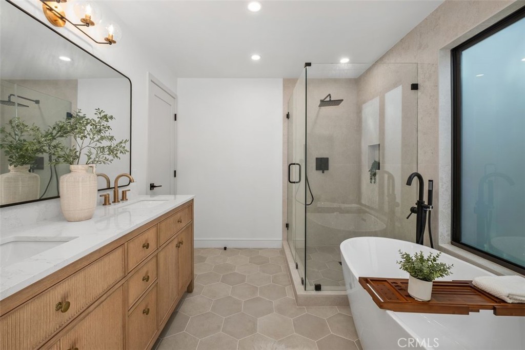 Bathroom with a wood double vanity, glass shower, and freestanding tub beside a large window.
