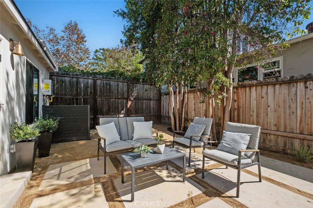 Fenced backyard patio with cushioned seating beneath a mature tree.